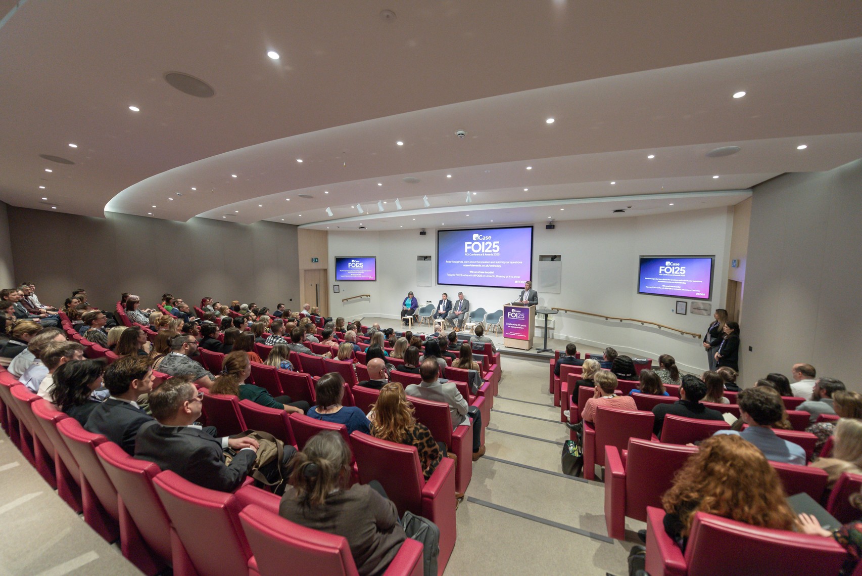 Wide shot of FOI25 conference room - rows of people watching a presentation